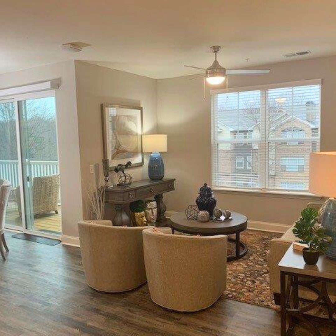 A bright and stylishly decorated living room with large windows, neutral-toned furniture, and a decorative console table.