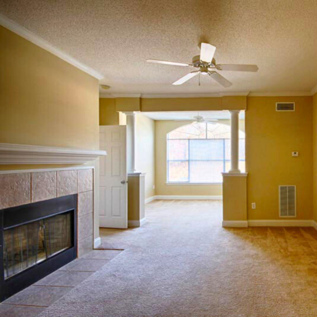A spacious interior featuring a tiled fireplace and an arched transition into a sunlit room with a large window.