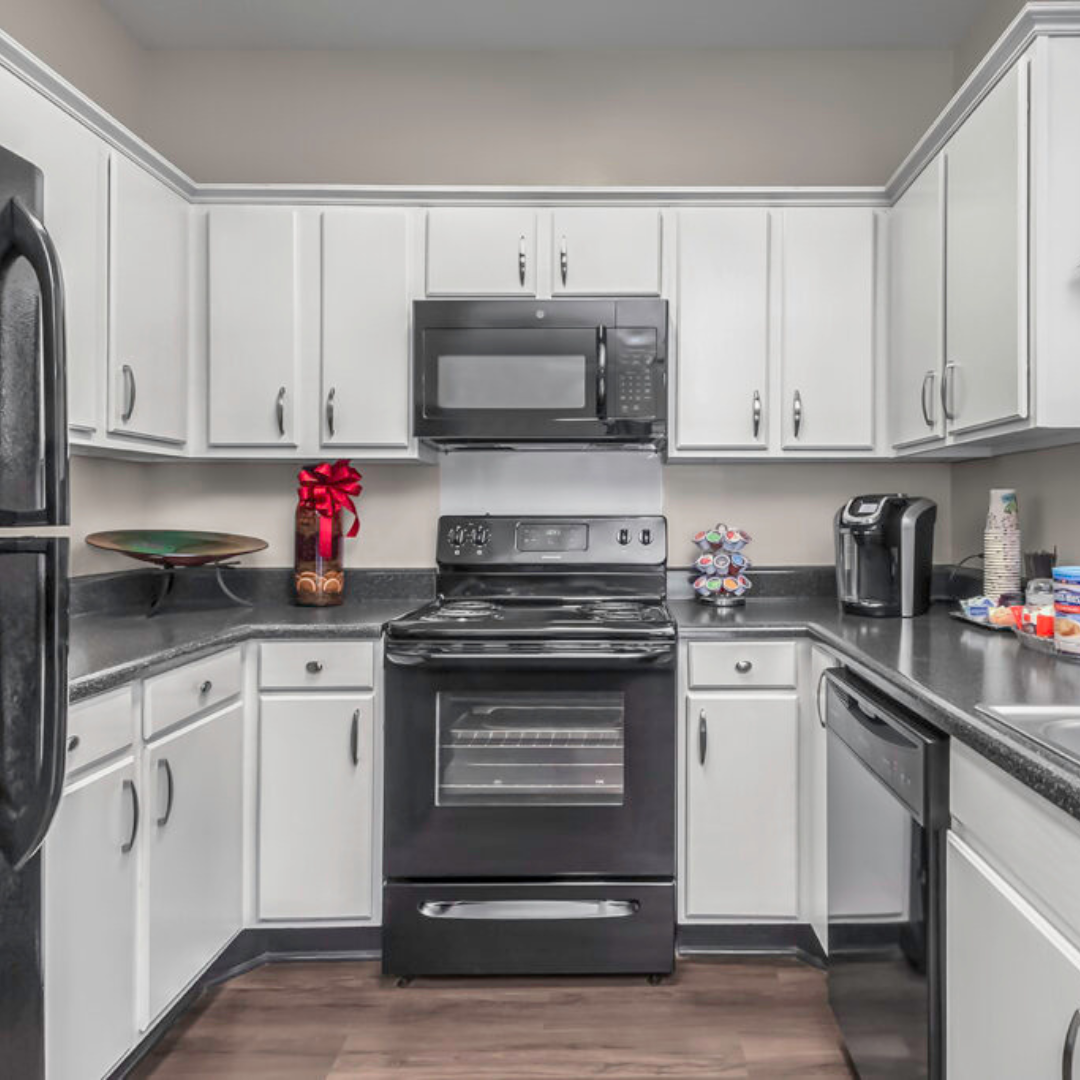 A clean, modern kitchen with white cabinetry, dark countertops, and black appliances, including a range and over-the-range microwave.